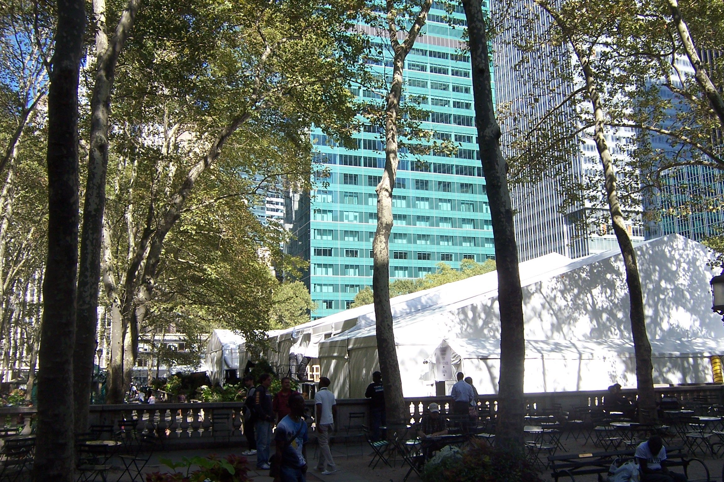 White event tents set up among the trees of Bryant Park in New York, with office towers rising behind them