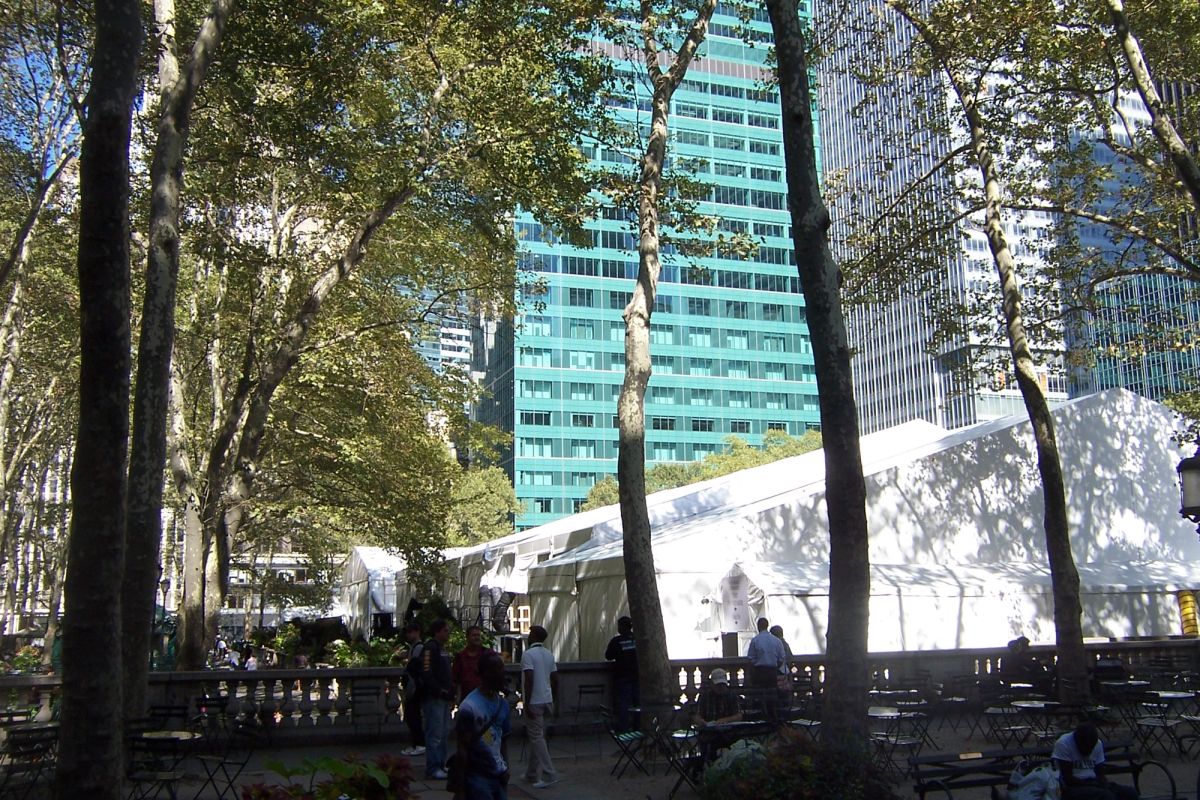 White event tents set up among the trees of Bryant Park in New York, with office towers rising behind them