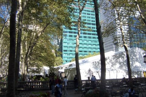 White event tents set up among the trees of Bryant Park in New York, with office towers rising behind them