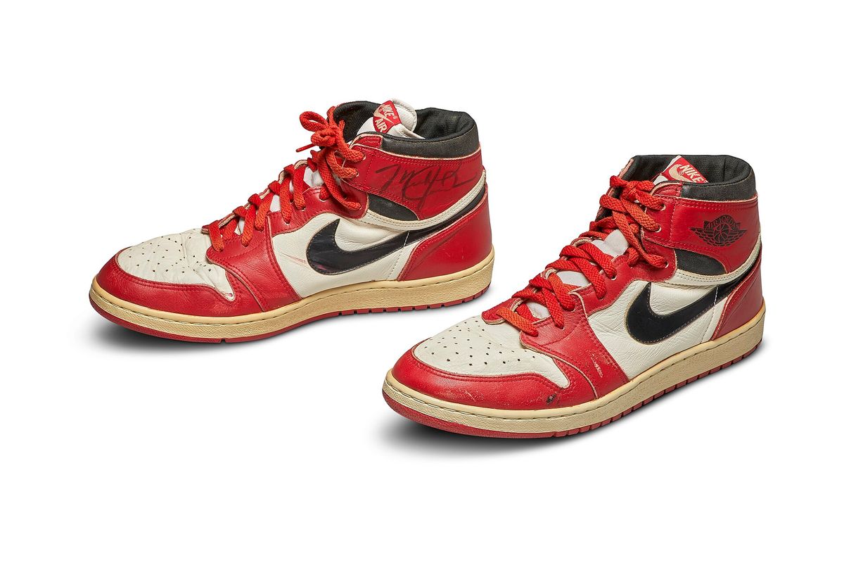 A pair of red, white and black Air Jordan 1 high-top sneakers with black swooshes and red laces, one signed in marker on the side, on a white background