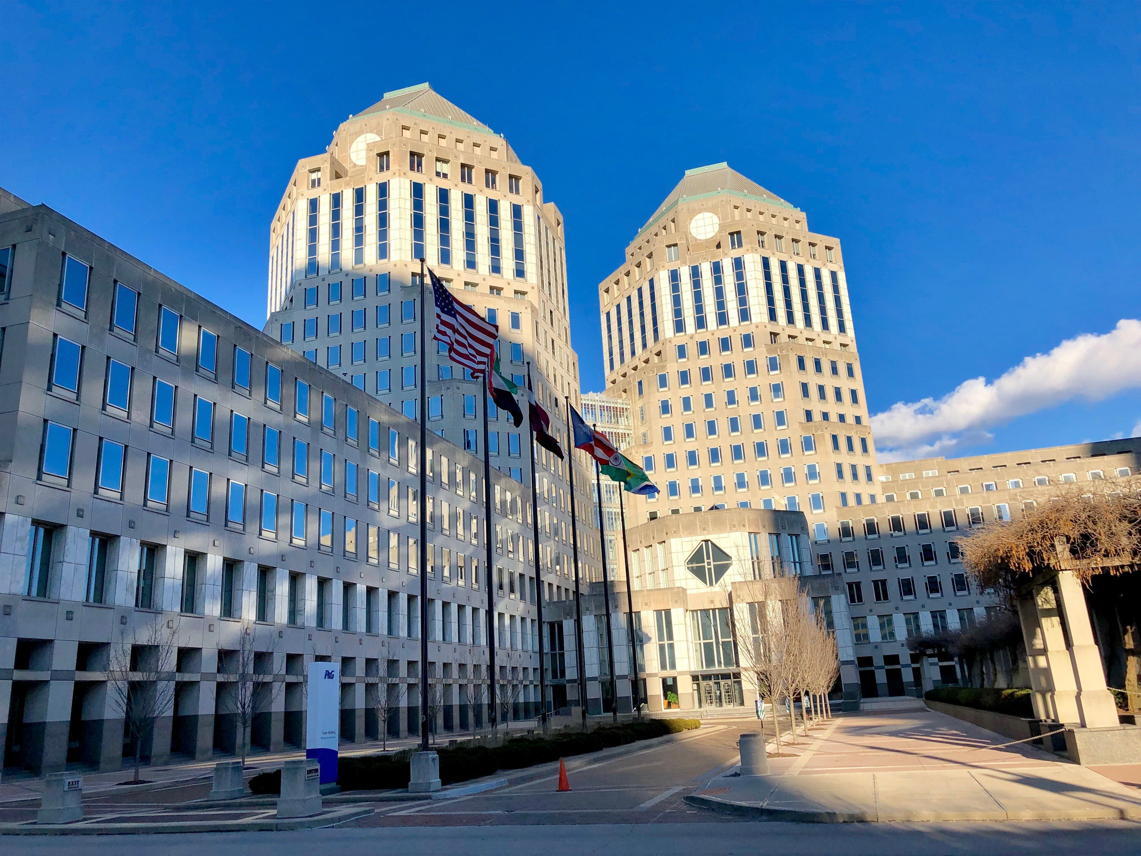 The twin towers of Procter & Gamble's world headquarters in Cincinnati under a blue sky, with flags flying on poles in the forecourt