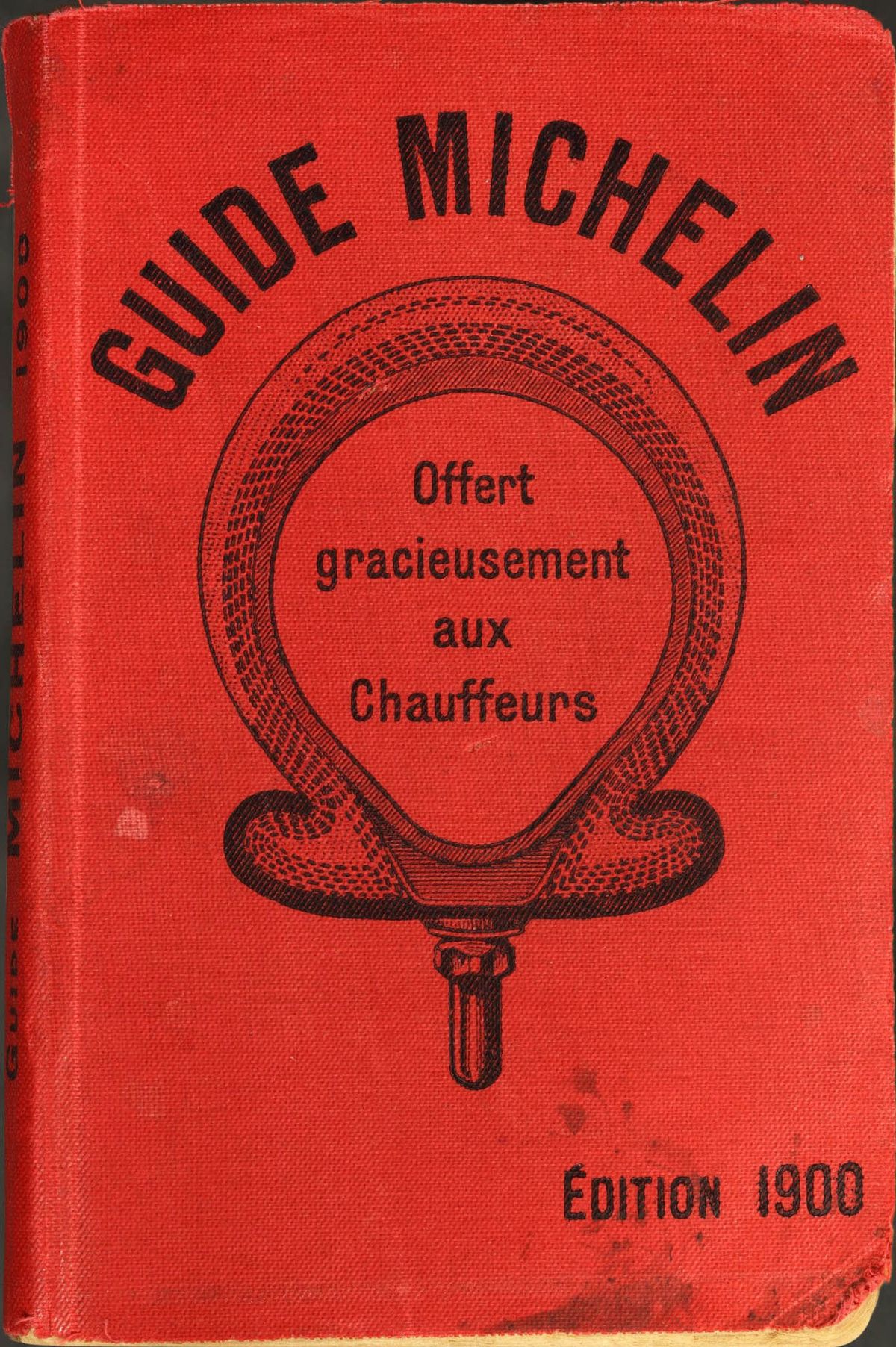 The red cloth cover of the first Michelin Guide, 1900, printed with a tire and the words "Offert gracieusement aux chauffeurs"