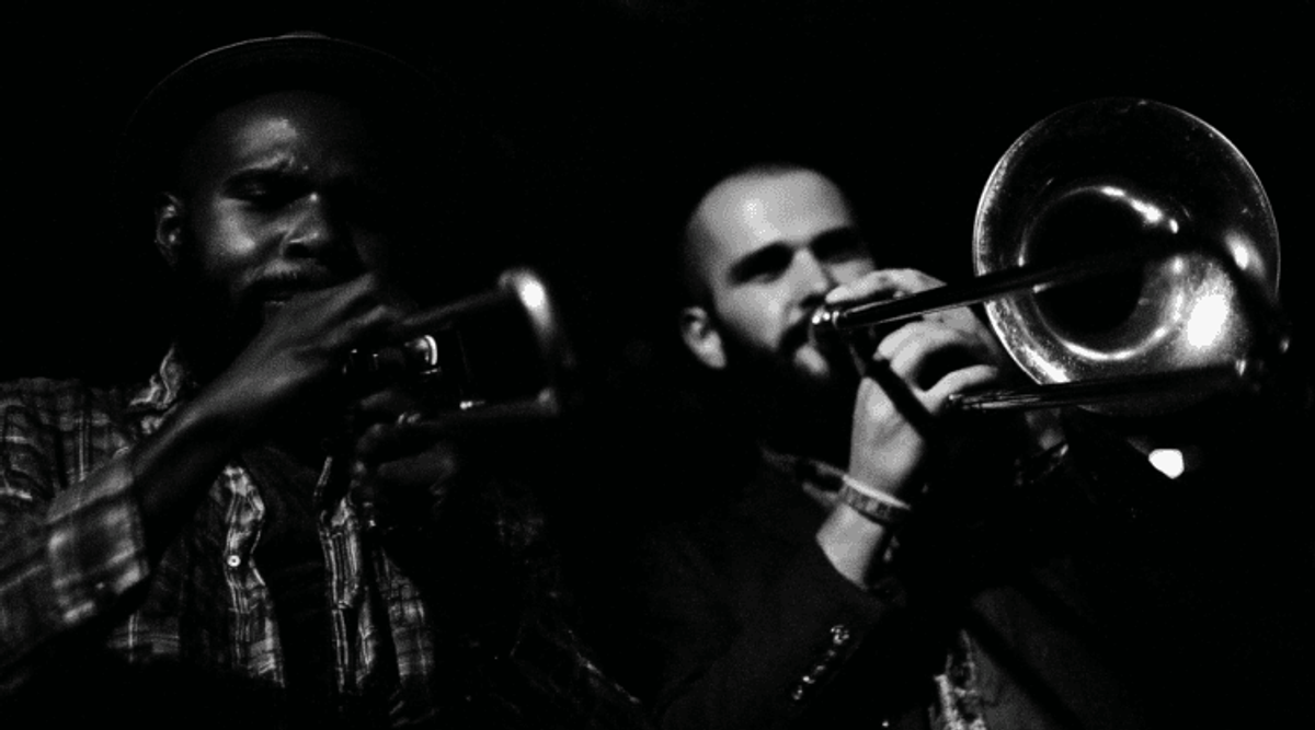 Musicians playing trumpet and trombone in dim lighting.