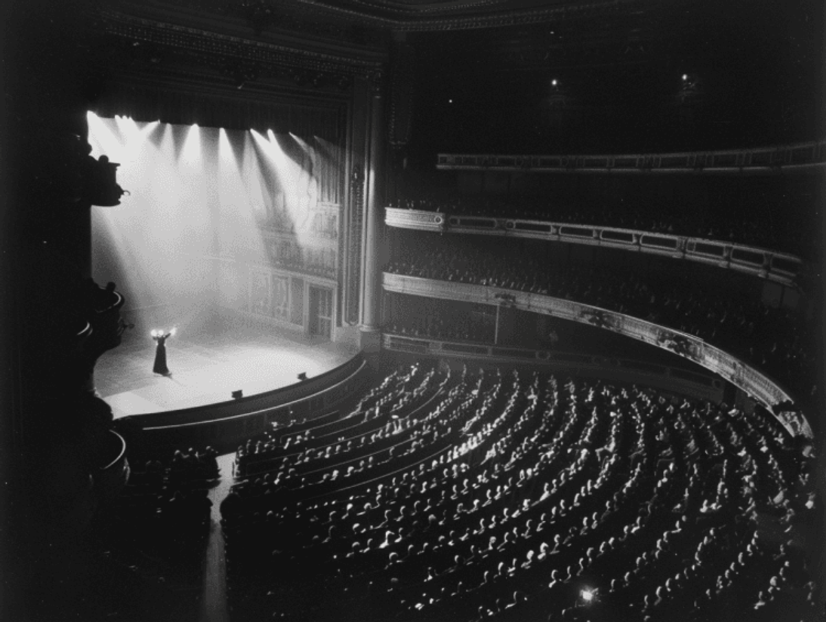 Performer onstage in grand theater before audience