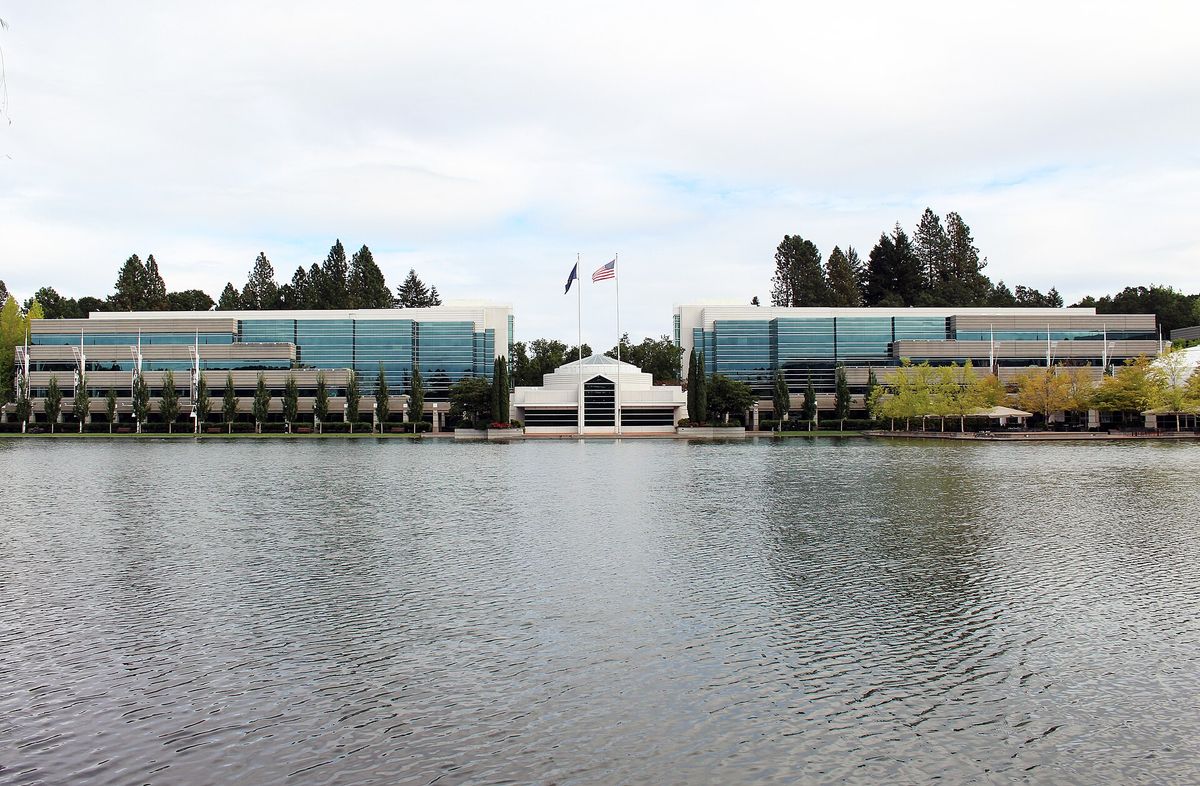 Nike World Headquarters in Beaverton, Oregon, seen across a lake: two long glass office buildings among evergreen trees under an overcast sky
