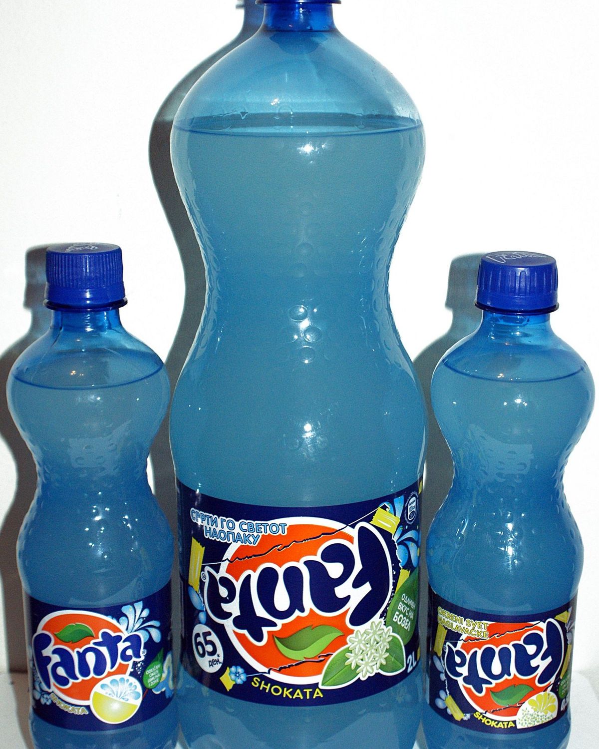 Three plastic bottles of Fanta Shokata, one large and two small, with blue caps and blue and orange labels