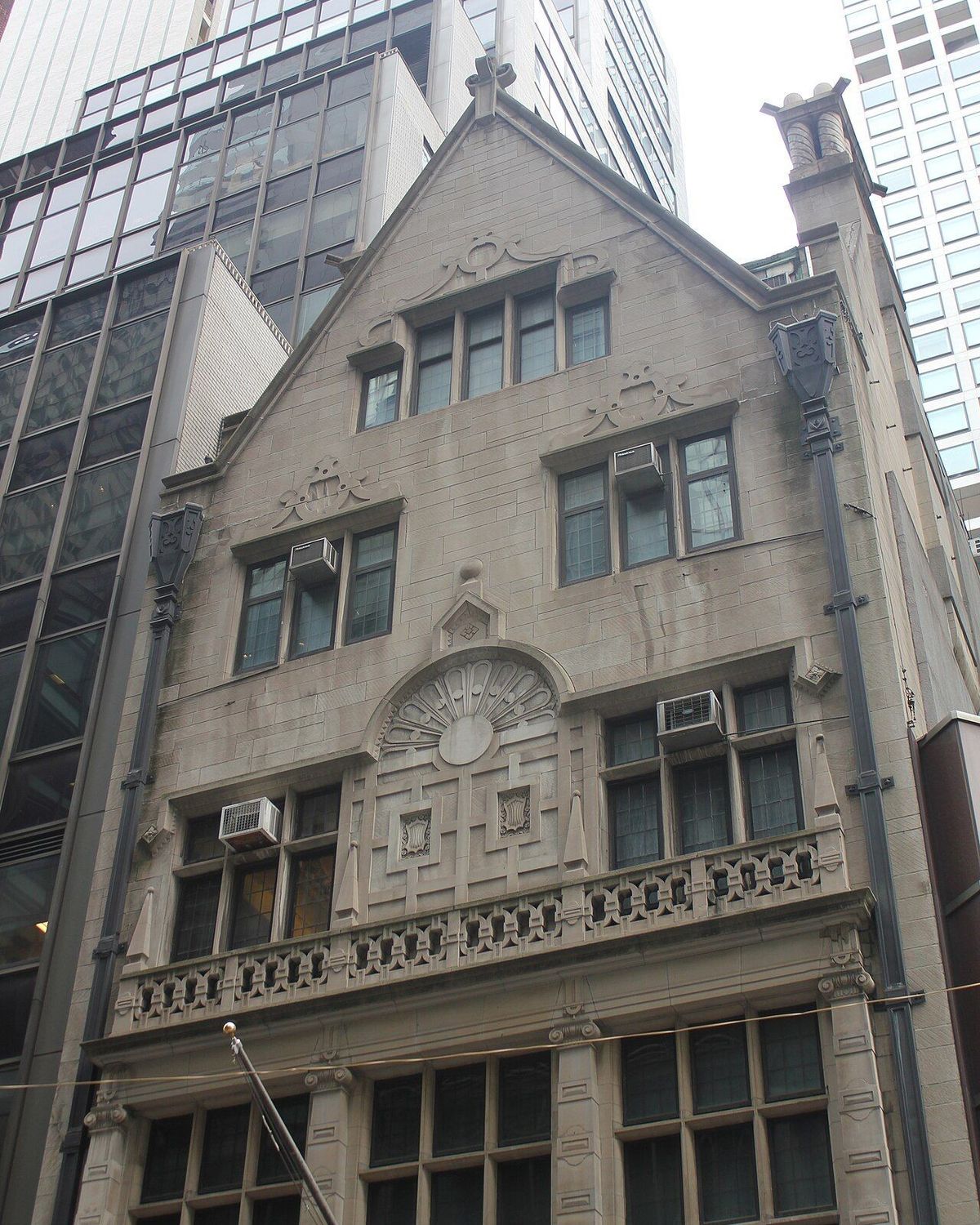 The stone facade of the Martin Erdmann House on East 55th Street, with a steep gable, a carved fan ornament and a balustrade, between glass office towers