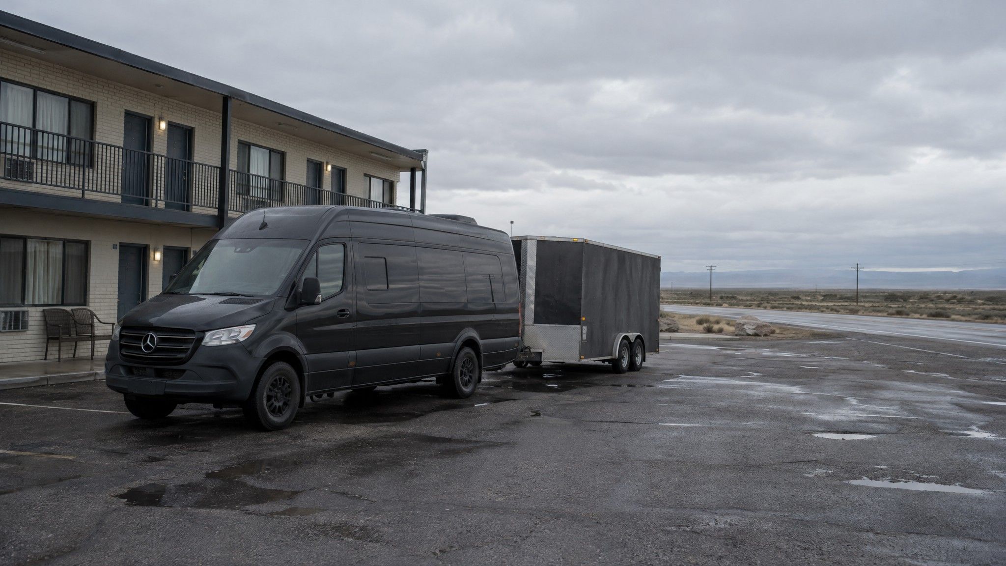 Tour van with a trailer parked at a roadside motel, overcast