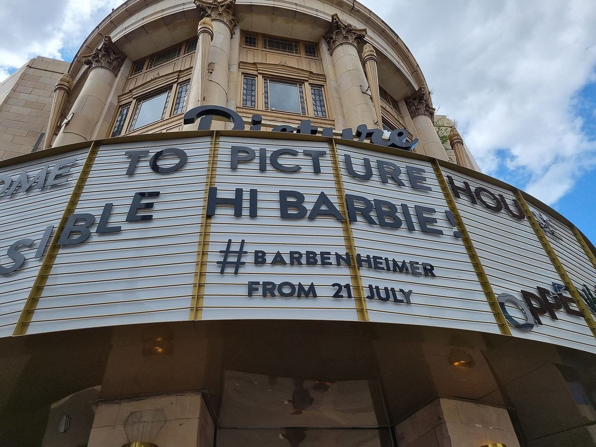 A curved cinema marquee reading Hi Barbie! and #Barbenheimer from 21 July, seen from below against a blue sky