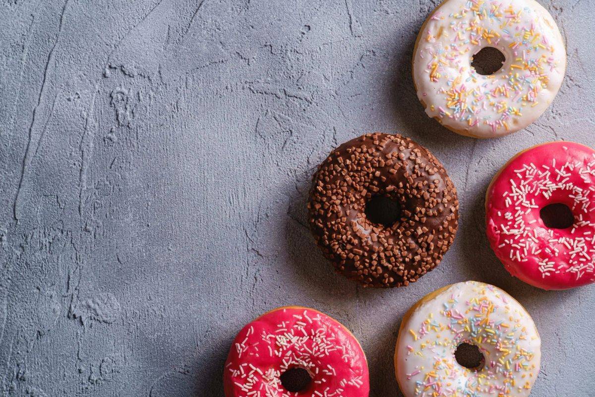 Five donuts with sprinkles, two pink, two white and one chocolate, on a grey concrete surface