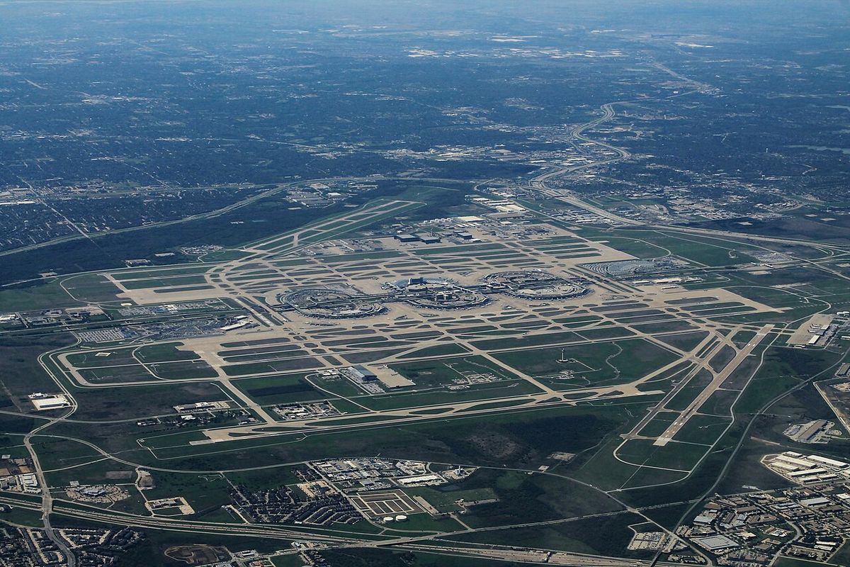 Aerial view of Dallas Fort Worth International Airport with its semicircular terminals, taxiways and runways surrounded by flat green land