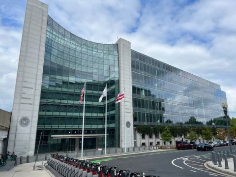 The curved glass entrance of the US Securities and Exchange Commission headquarters in Washington, with three flags out front and a row of docked bicycles in the foreground