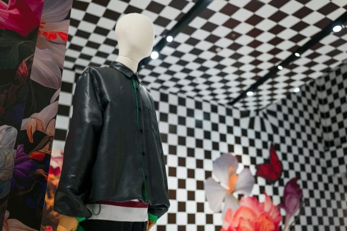 Mannequin in black jacket, checkered room background.