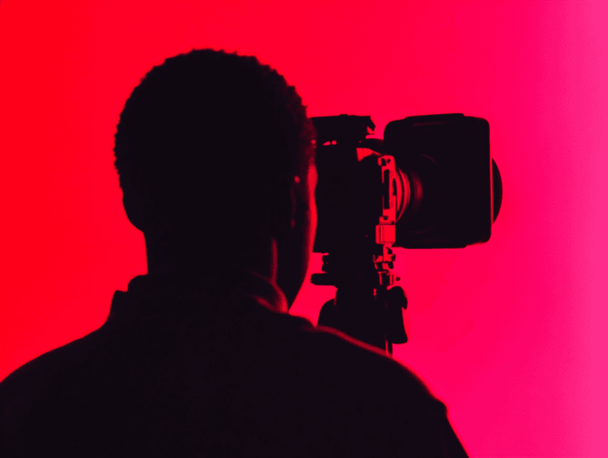 Silhouetted person filming against red backdrop