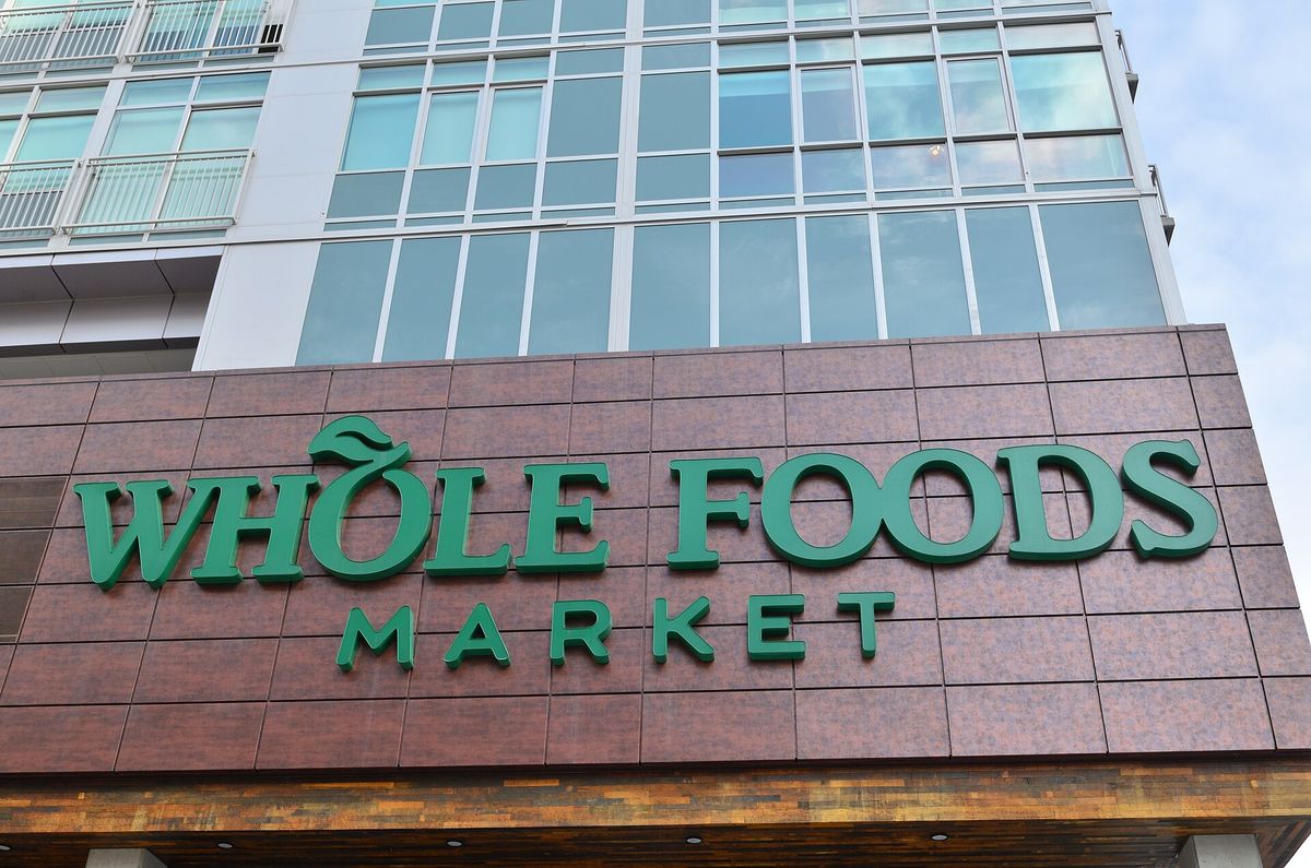 Green Whole Foods Market lettering on a brown stone facade below the glass windows of a multi-story residential building