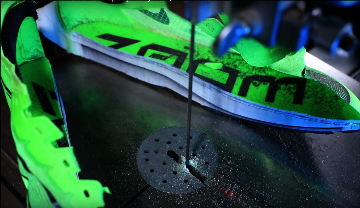 A bright green Nike Vaporfly running shoe being cut lengthwise on a band saw, showing the white foam midsole