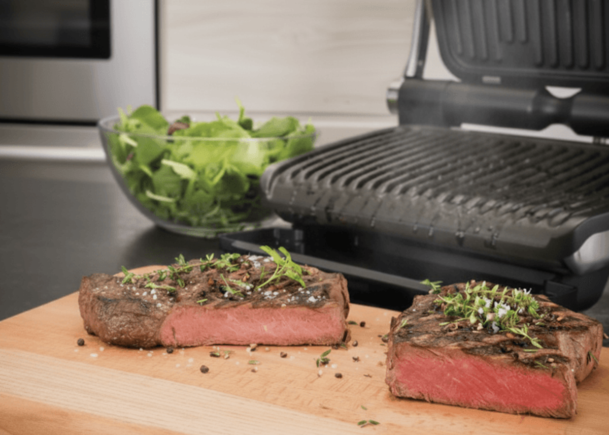 Grilled steak slices with fresh herbs on cutting board.