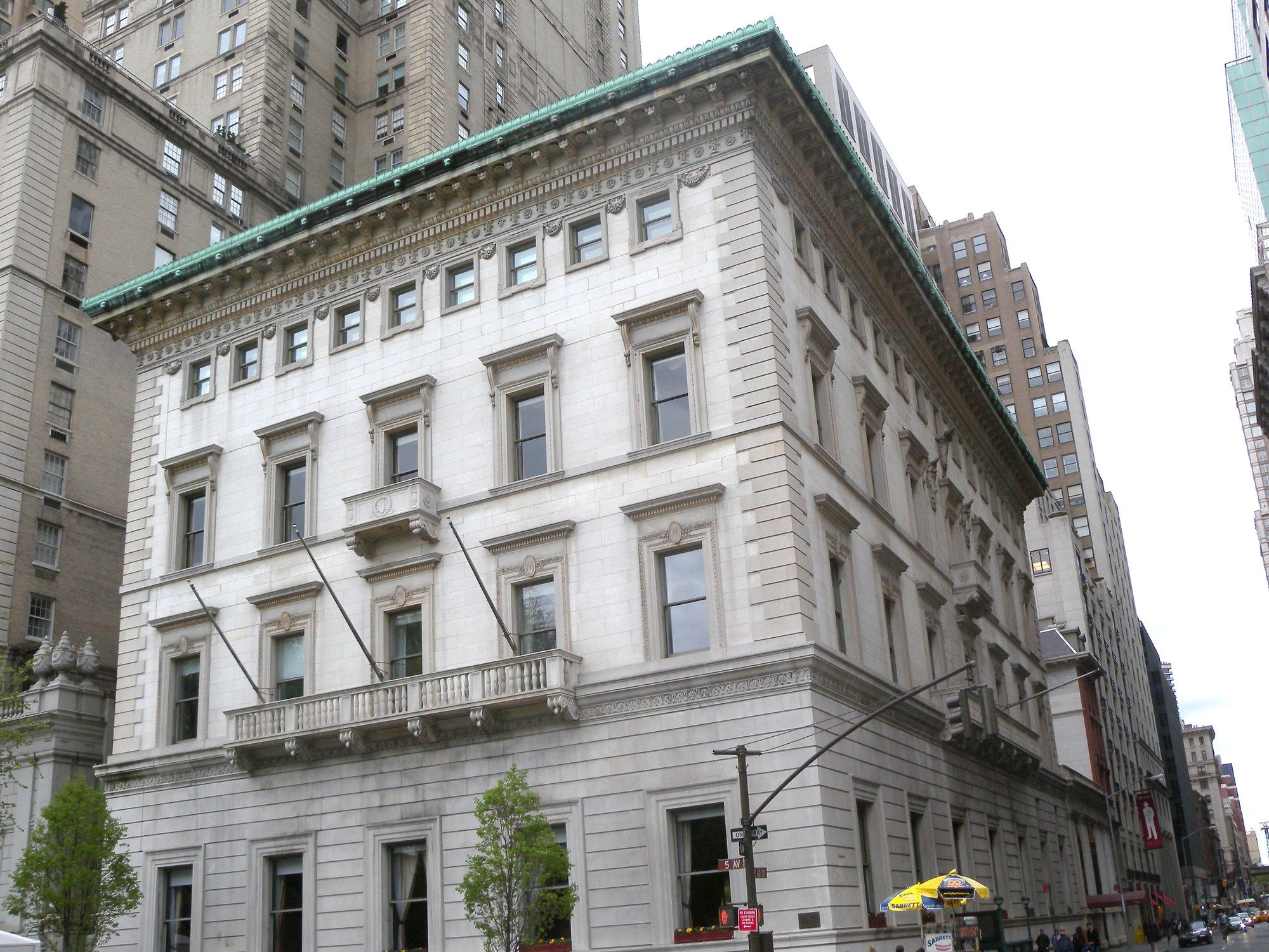 The Metropolitan Club's white marble clubhouse at Fifth Avenue and 60th Street, with a balcony above the ground floor and a green copper cornice, seen from the street corner