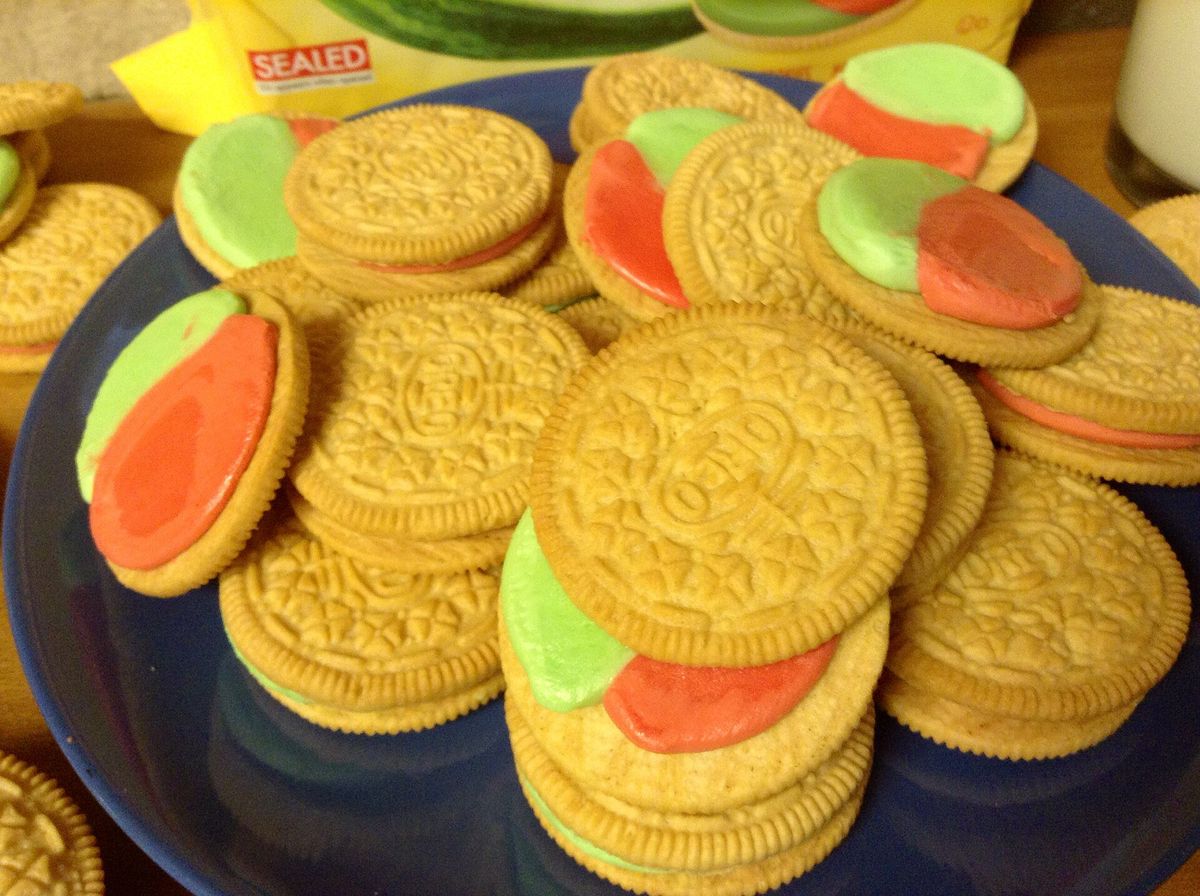 A plate of golden sandwich cookies filled with half green and half pink creme, several pulled apart to show the two-color filling