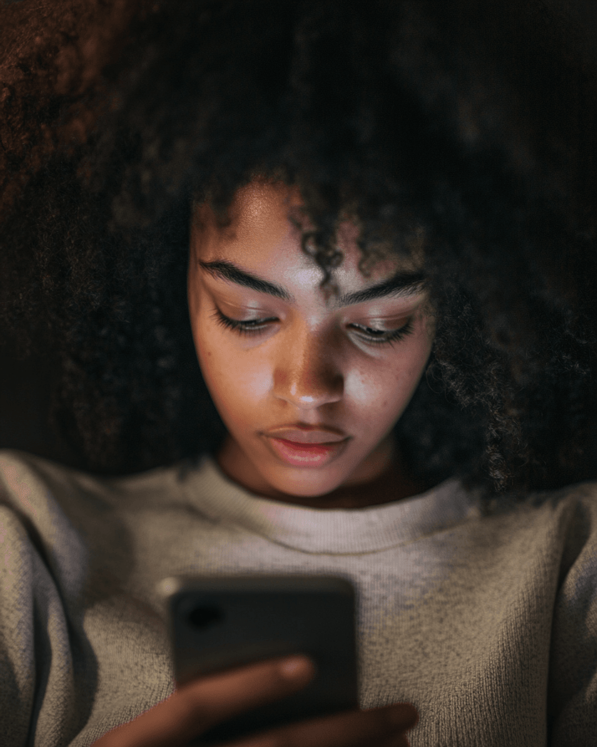 Person focused on smartphone screen in dim light.