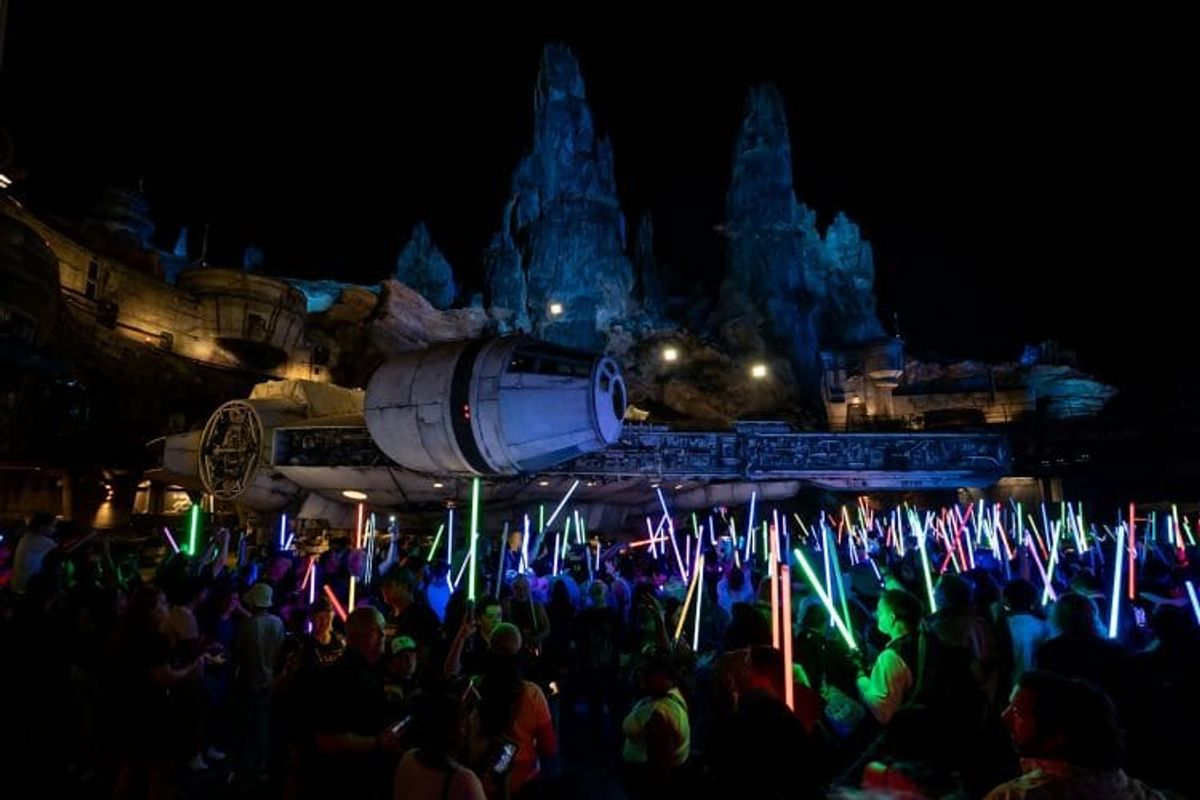 Crowd with lightsabers near spacecraft at night.