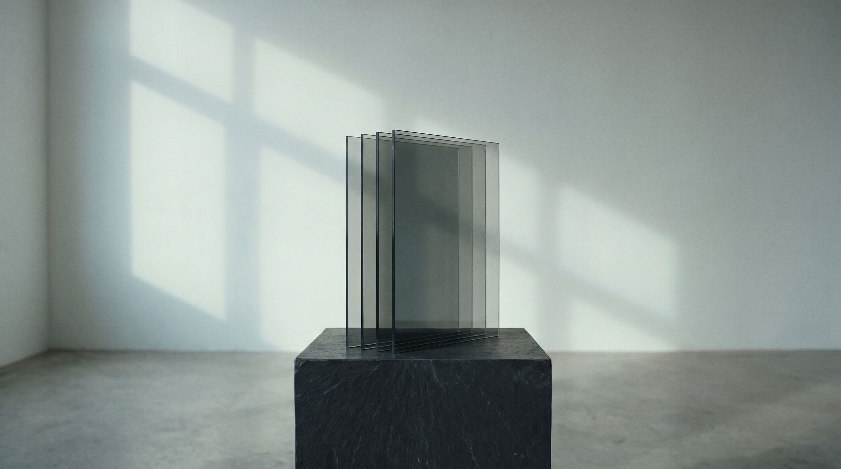 Four panes of smoked glass standing in layers on a slate plinth in soft window light