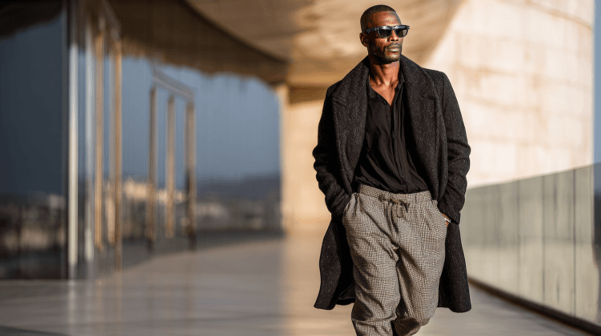 Fashionable man walking in stylish outfit and sunglasses.