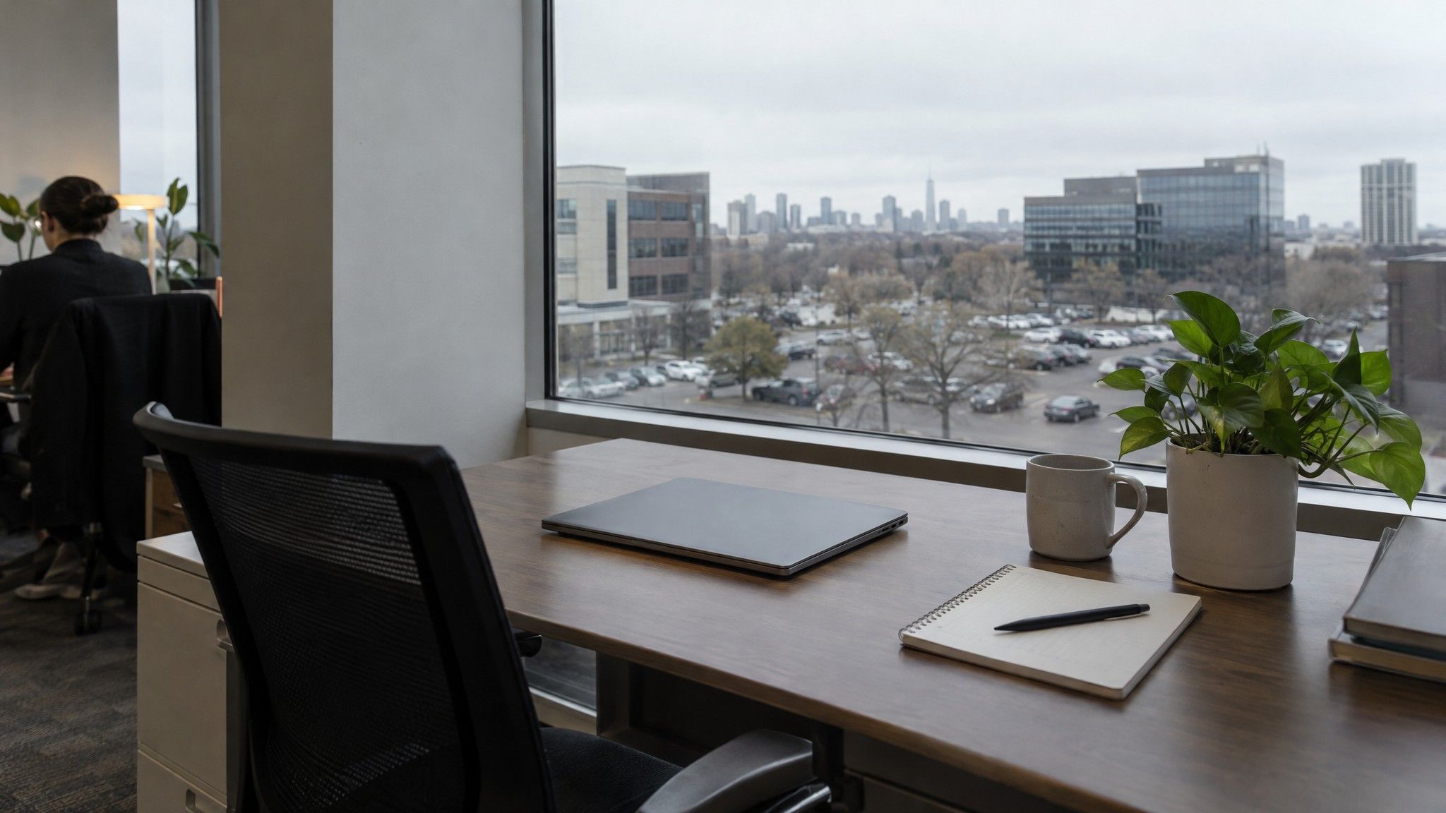 Window desk with closed laptop, notebook and plant facing an office park