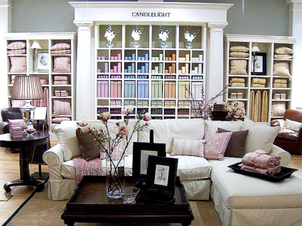 Store display with a white slipcovered sectional sofa, pink pillows and throws, and shelves of folded linens under a sign reading Candlelight