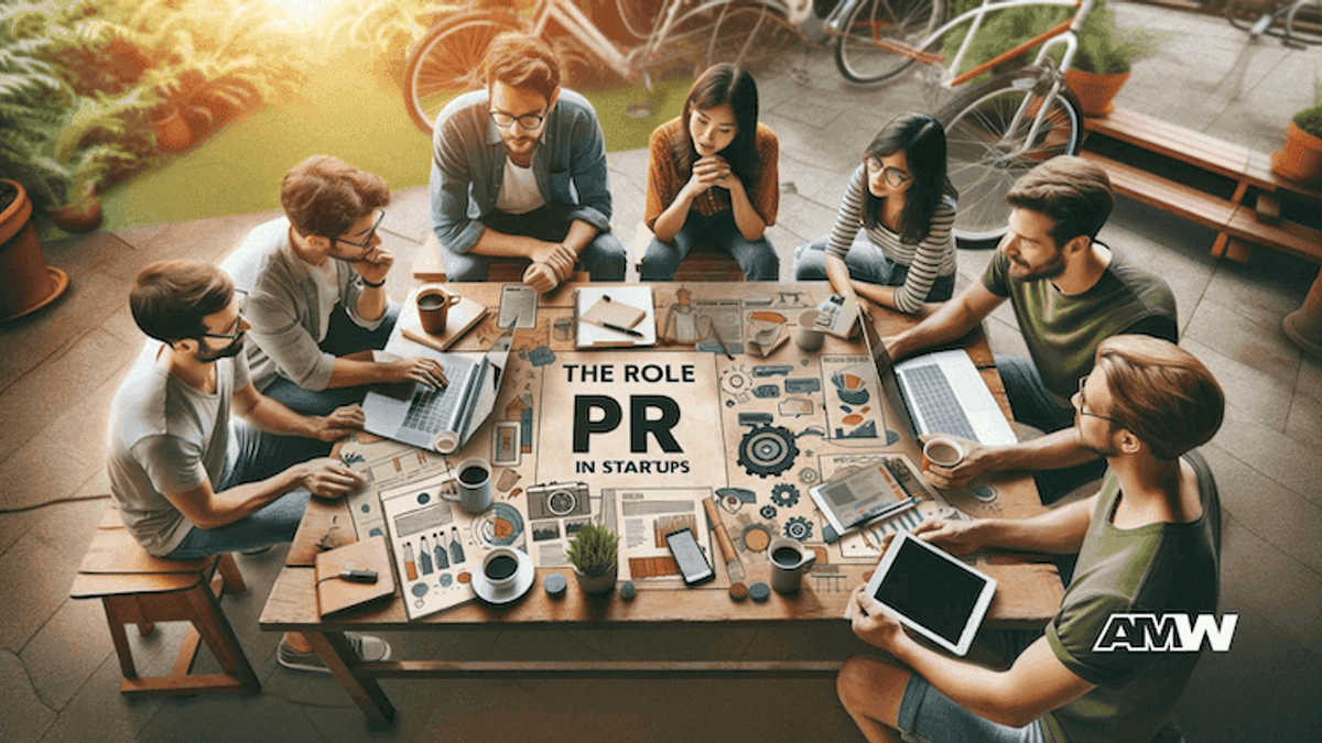 An outdoor table seen from above with people working on laptops and tablets around printed pages and a card reading THE ROLE OF PR IN STARTUPS.