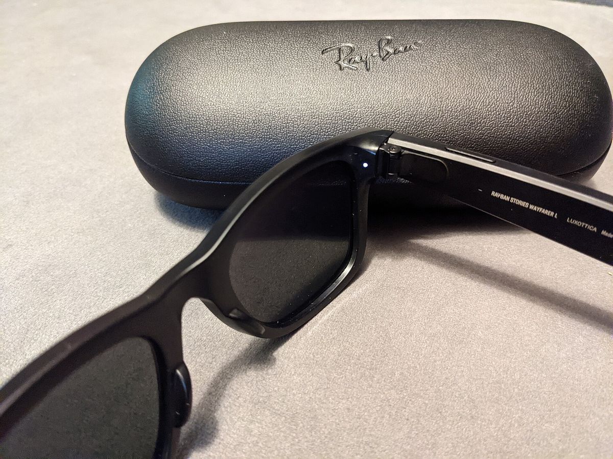 Close-up of the hinge area of black Ray-Ban Stories glasses with a small white LED lit, resting on a black Ray-Ban case