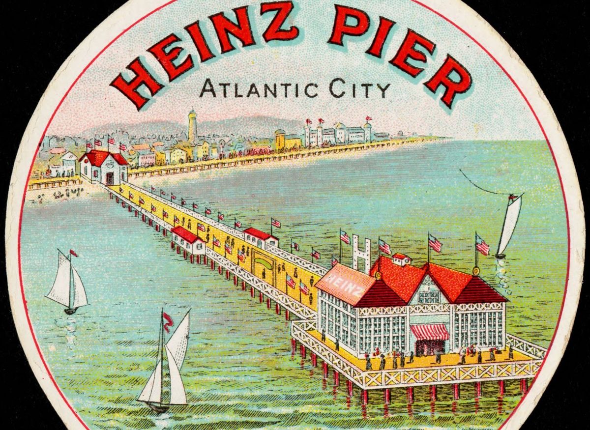 Color lithograph souvenir card reading Heinz Pier, Atlantic City, showing a long pier with flags leading out to a white pavilion with red roofs and the word Heinz, with sailboats on green water and the town along the shore behind