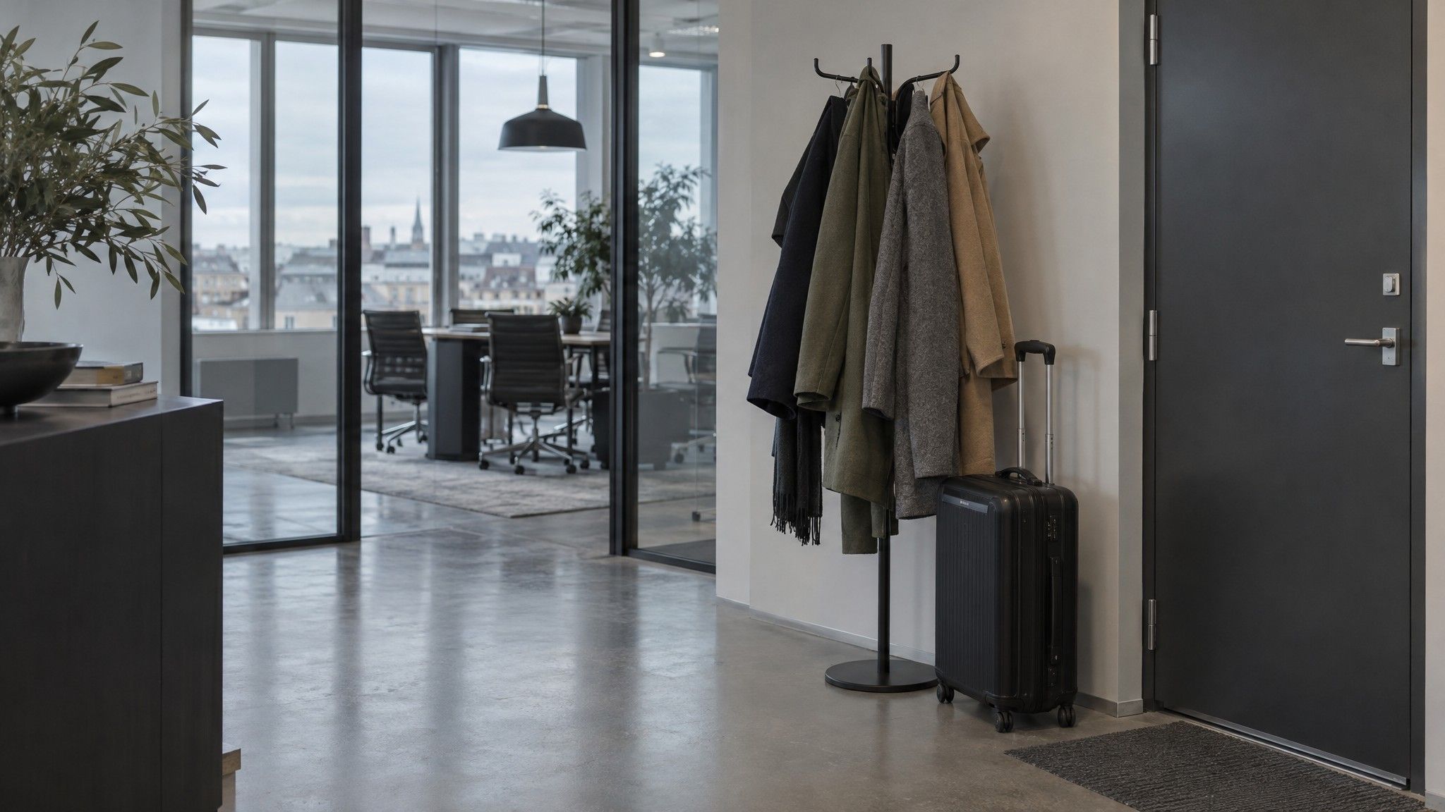 Office coat stand with several coats beside a single carry-on case