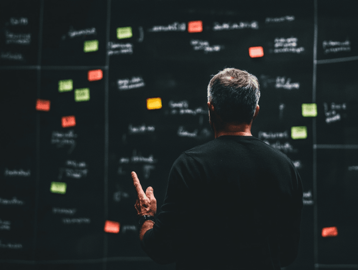 Man brainstorming with sticky notes on chalkboard.