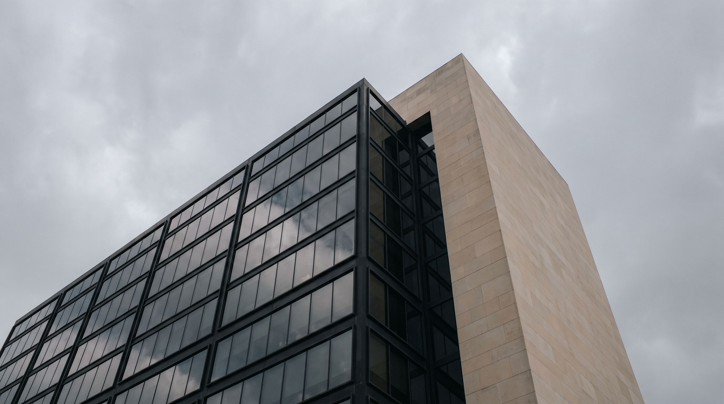 Dark glass office tower meeting a pale stone tower under an overcast sky