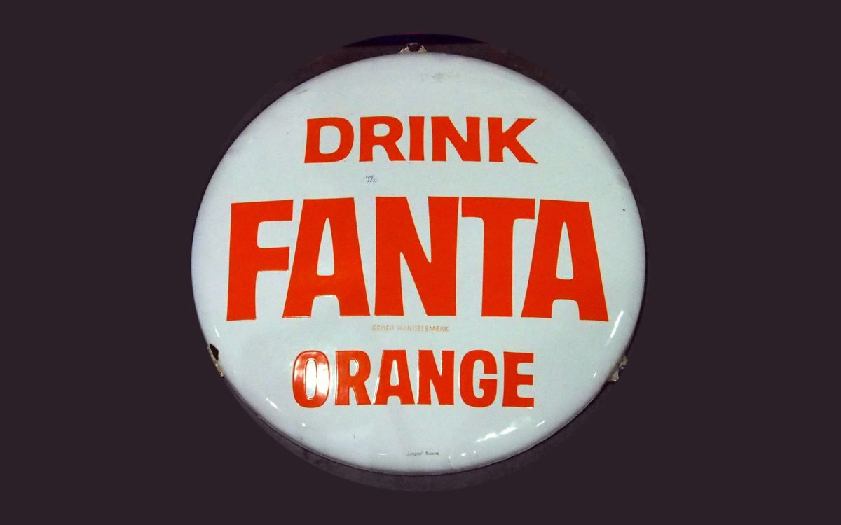 A round white enamel advertising sign reading Drink Fanta Orange in red capital letters, set against a dark background