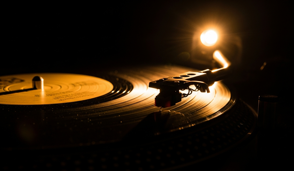 Vinyl record spinning on turntable with dramatic side lighting — comparing label services deals and traditional record label contracts