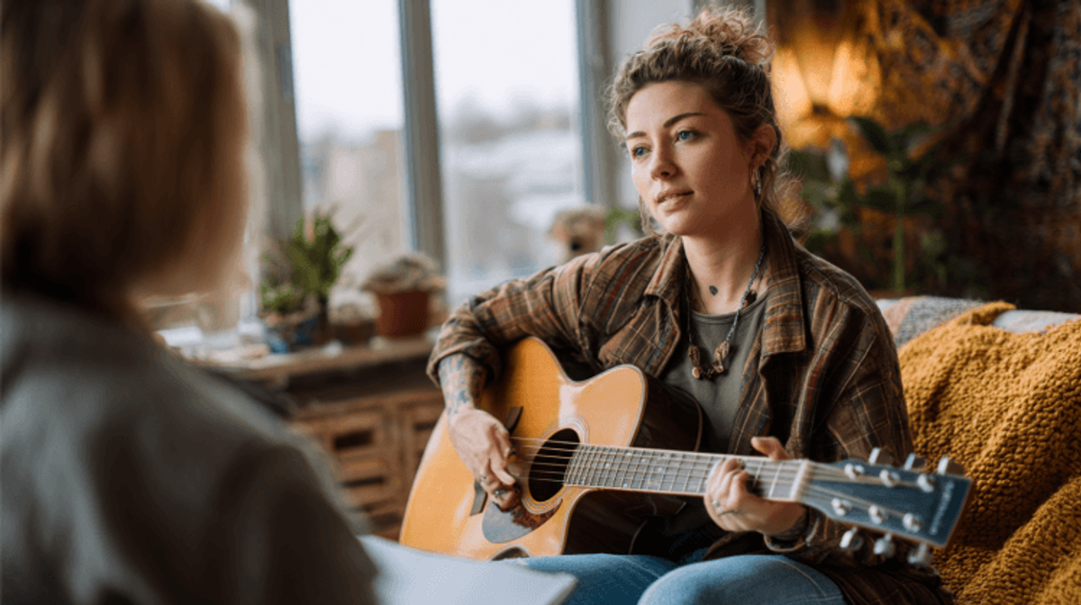 Woman playing guitar while speaking to another person.