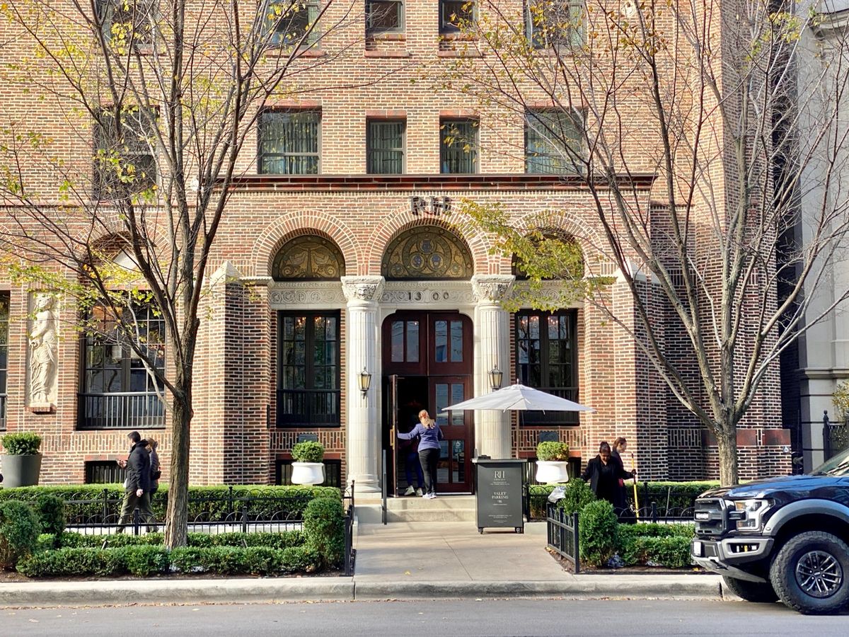 Brick entrance of the former Three Arts Club building in Chicago with an RH sign above the arched doorway, a doorman at the open door and a hedge-lined walk