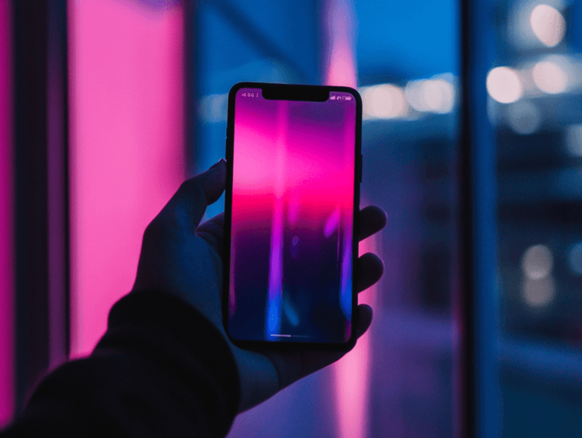 Hand holding smartphone with vibrant screen glow.