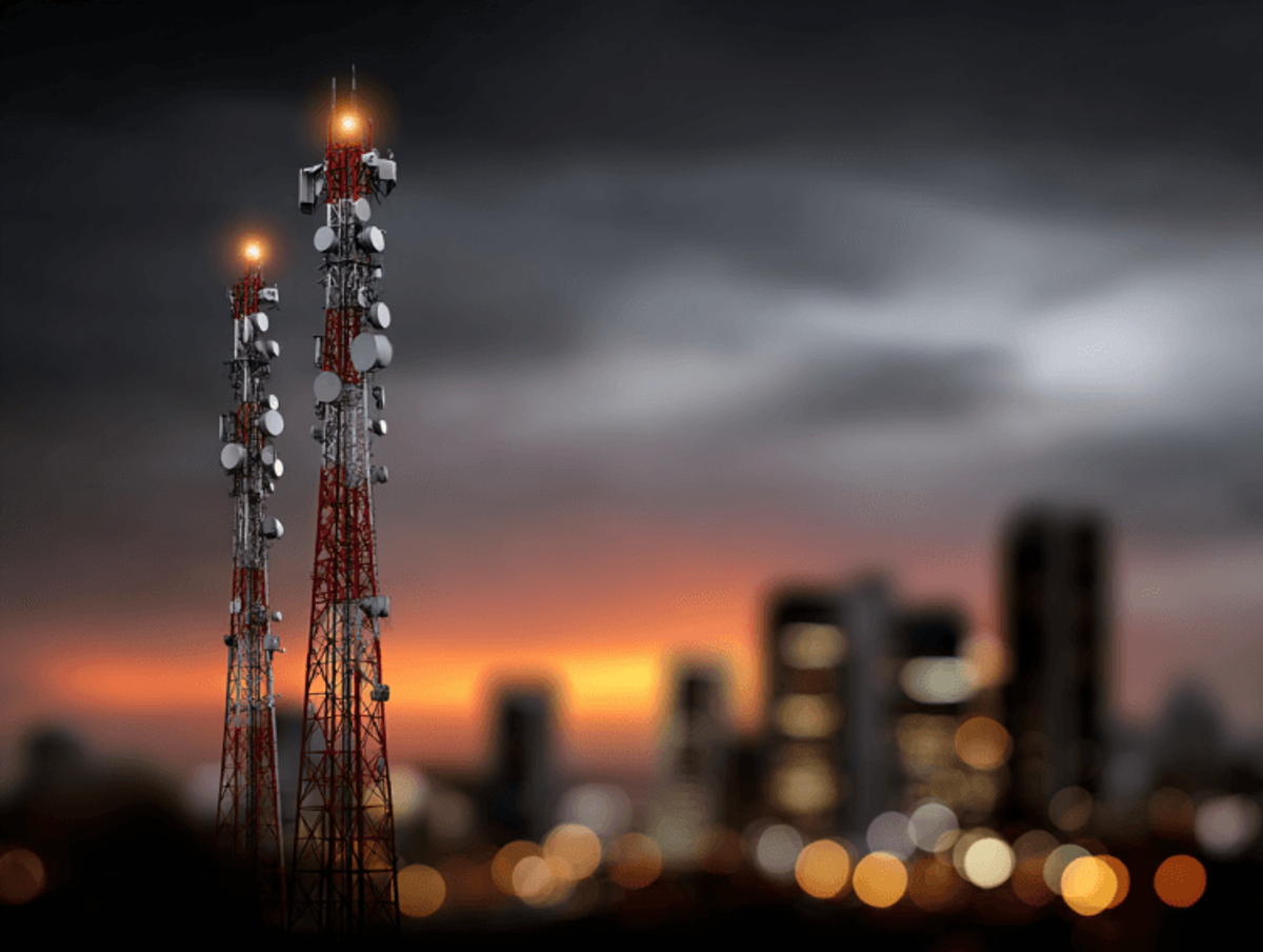 Cell towers at sunset with city skyline.