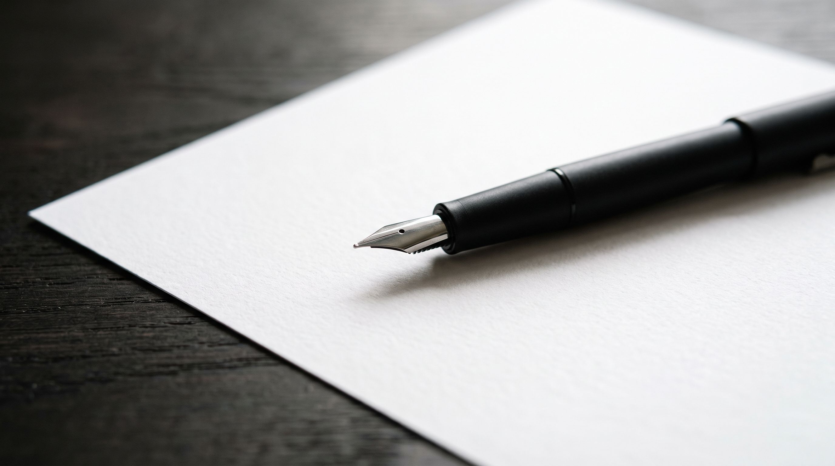 Black fountain pen resting on a blank sheet of white paper on a dark oak desk
