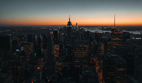 City skyline at twilight with warm building lights and deep shadows