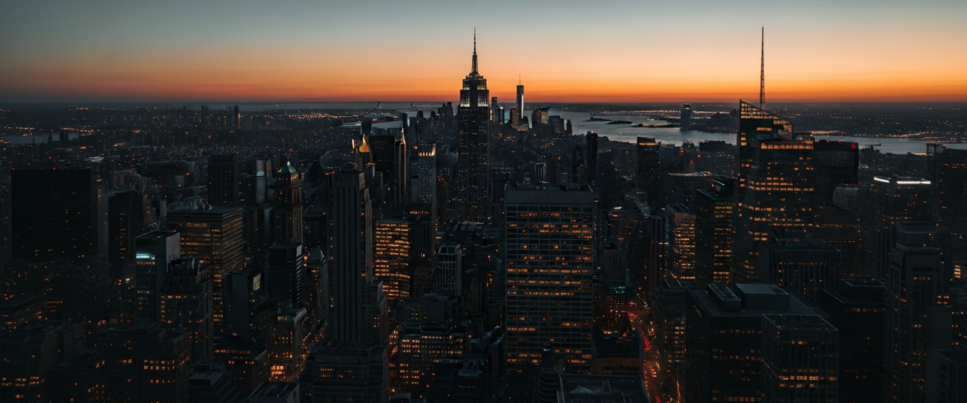 City skyline at twilight with warm building lights and deep shadows