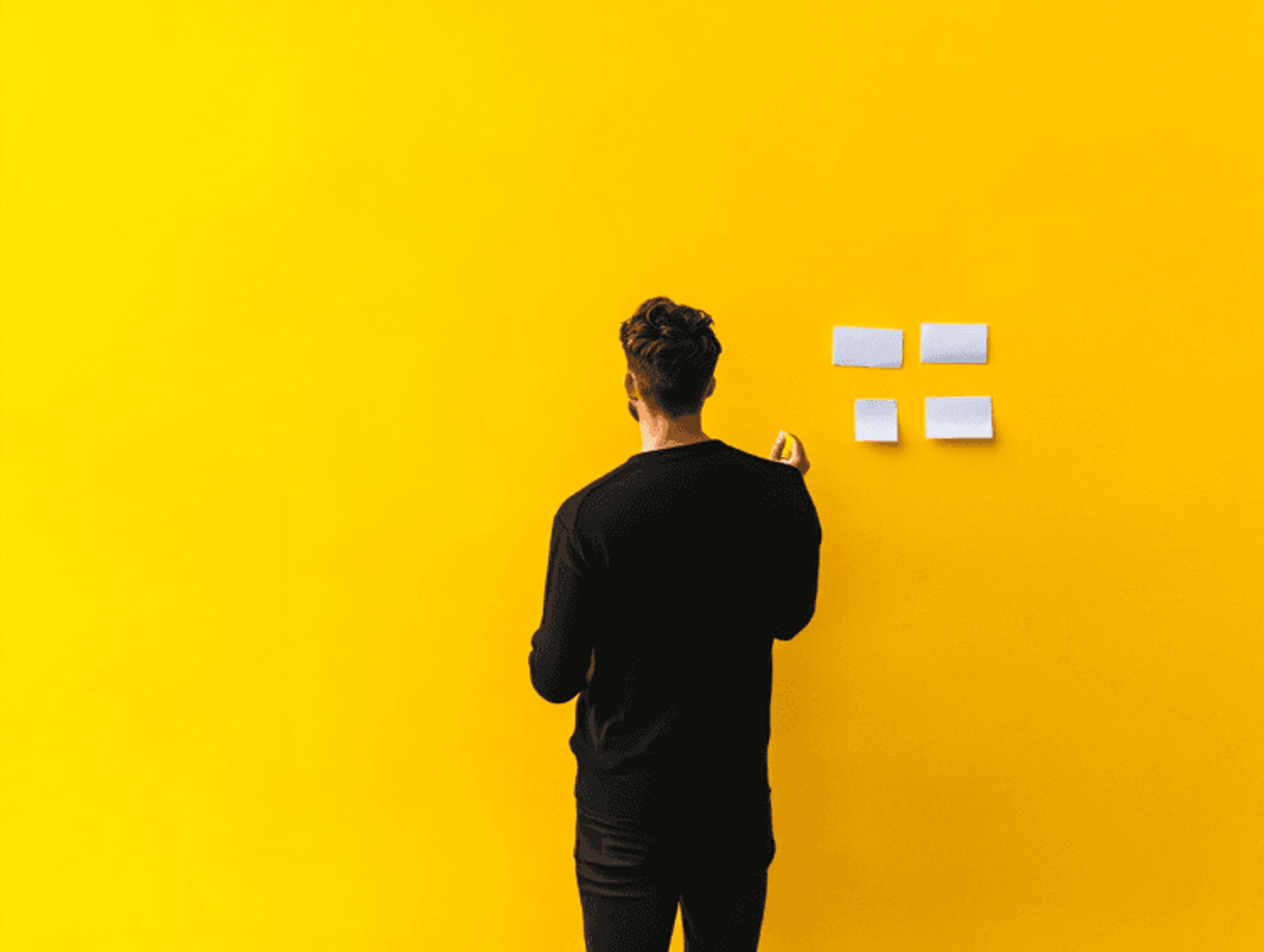 Person organizing sticky notes on yellow wall.