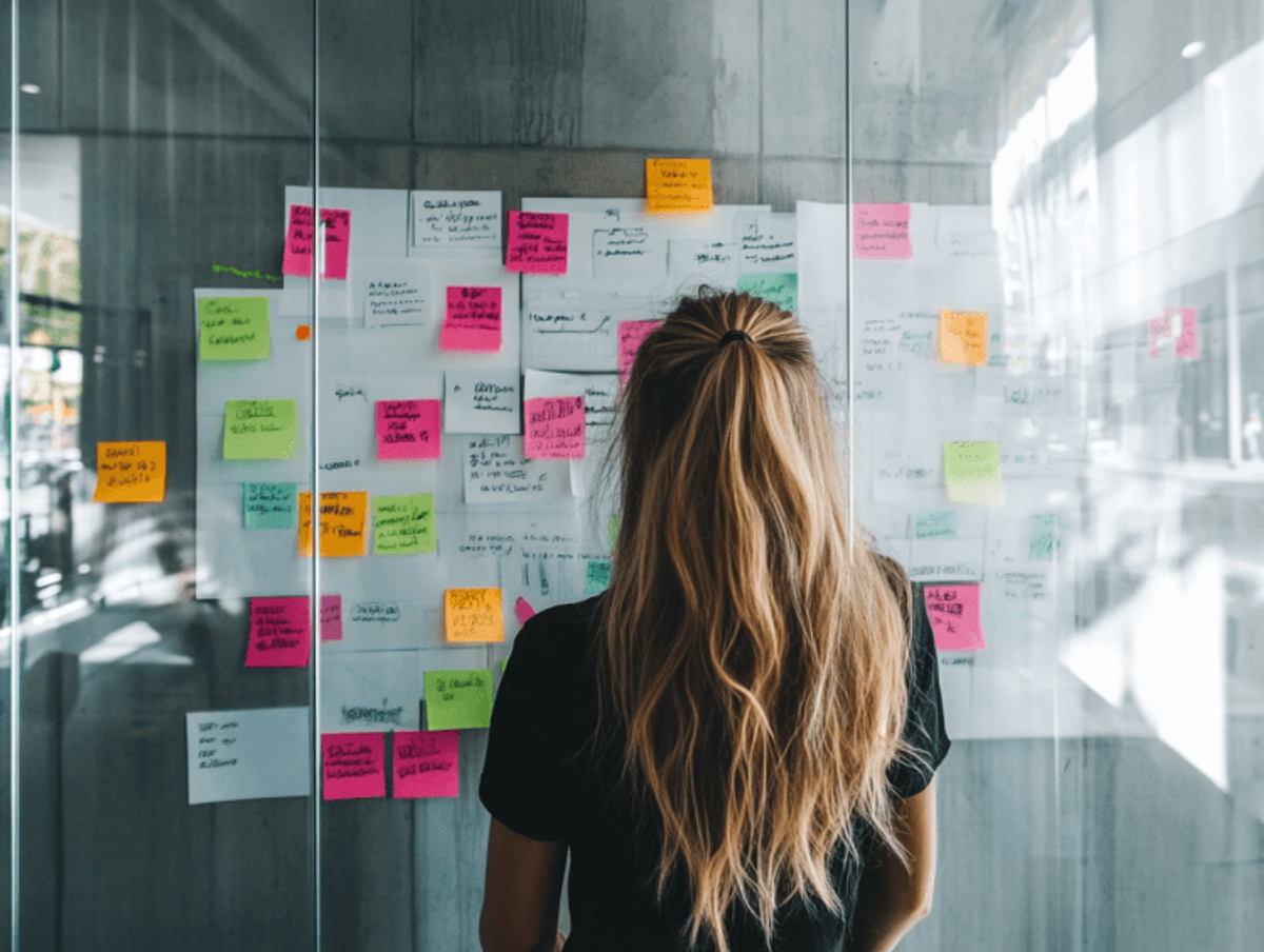 Woman reviewing colorful sticky notes on glass wall.