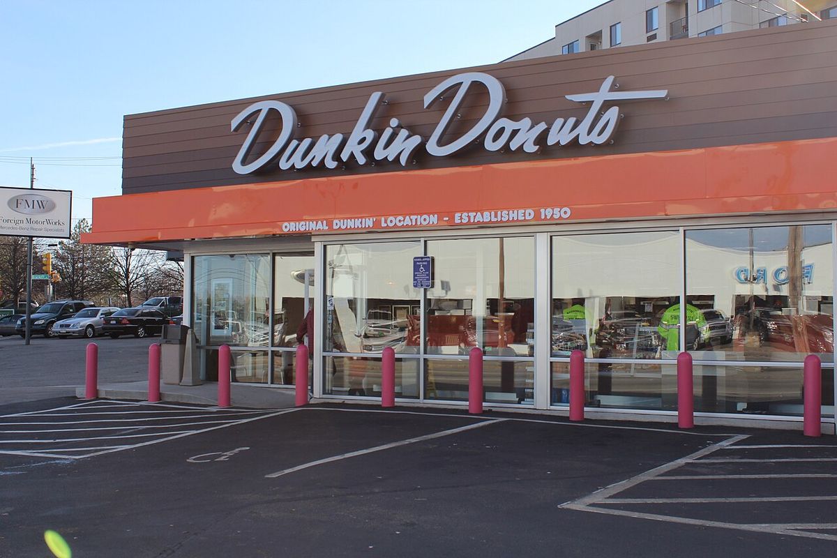 Storefront with a script Dunkin Donuts sign and an orange awning reading Original Dunkin' Location, Established 1950