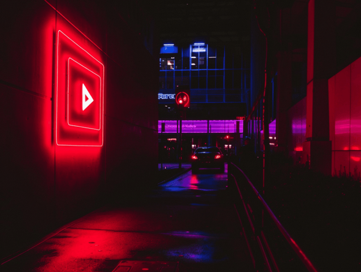 Neon play button in urban alley at night.