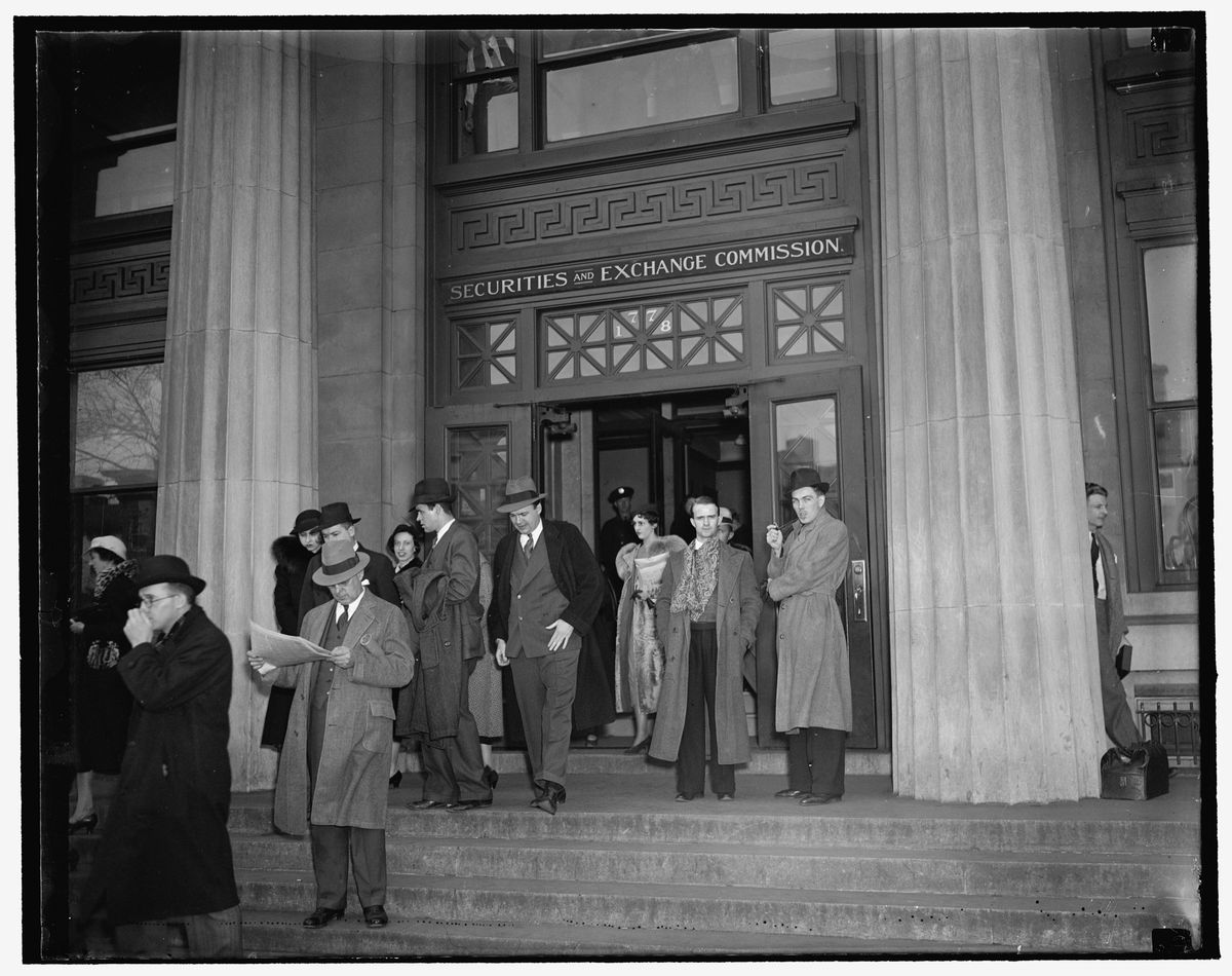 Men in hats and overcoats on the steps below a doorway lettered Securities and Exchange Commission, with a man reading a newspaper in the foreground