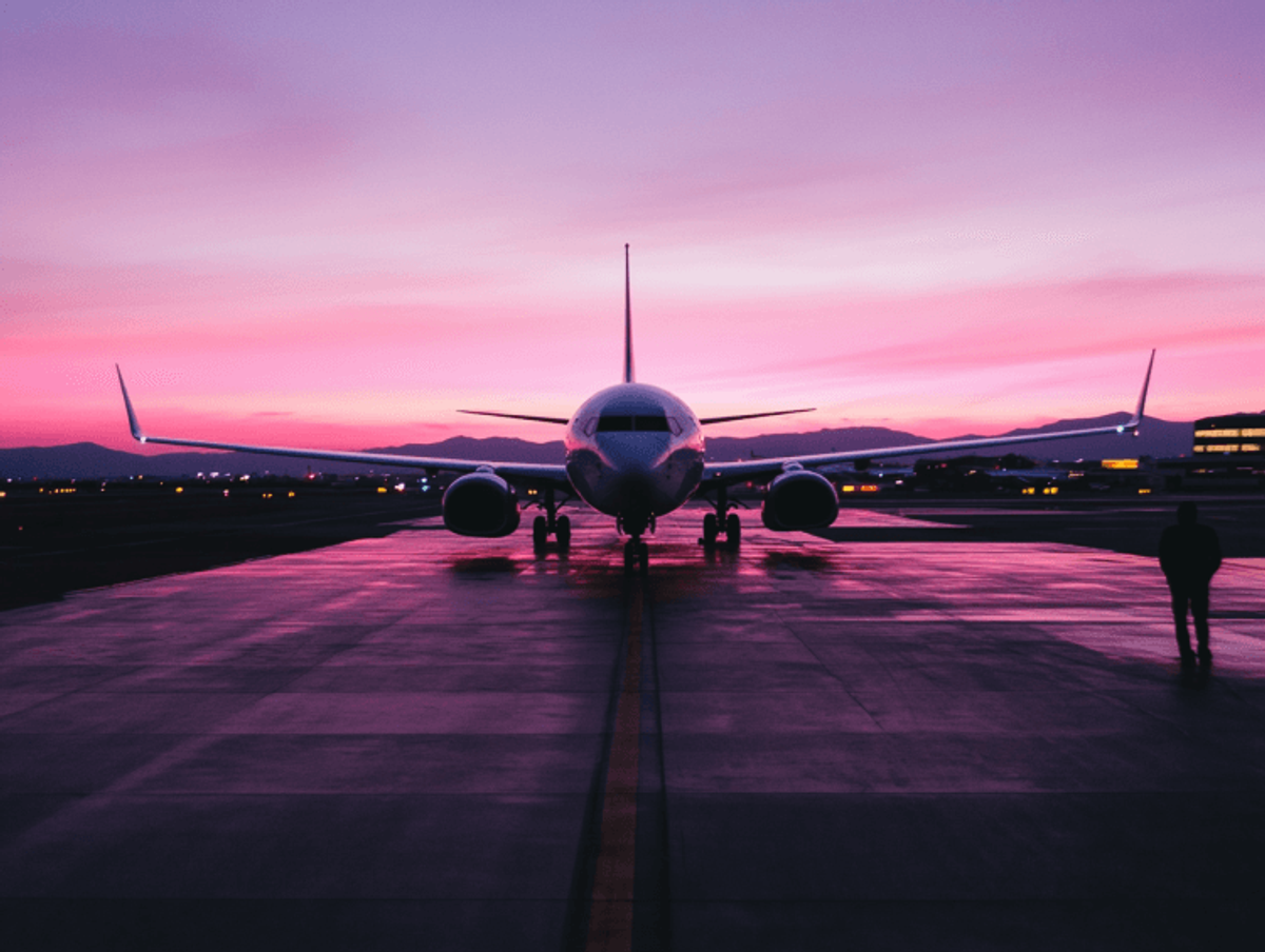 Airplane on runway at sunset, pink sky.